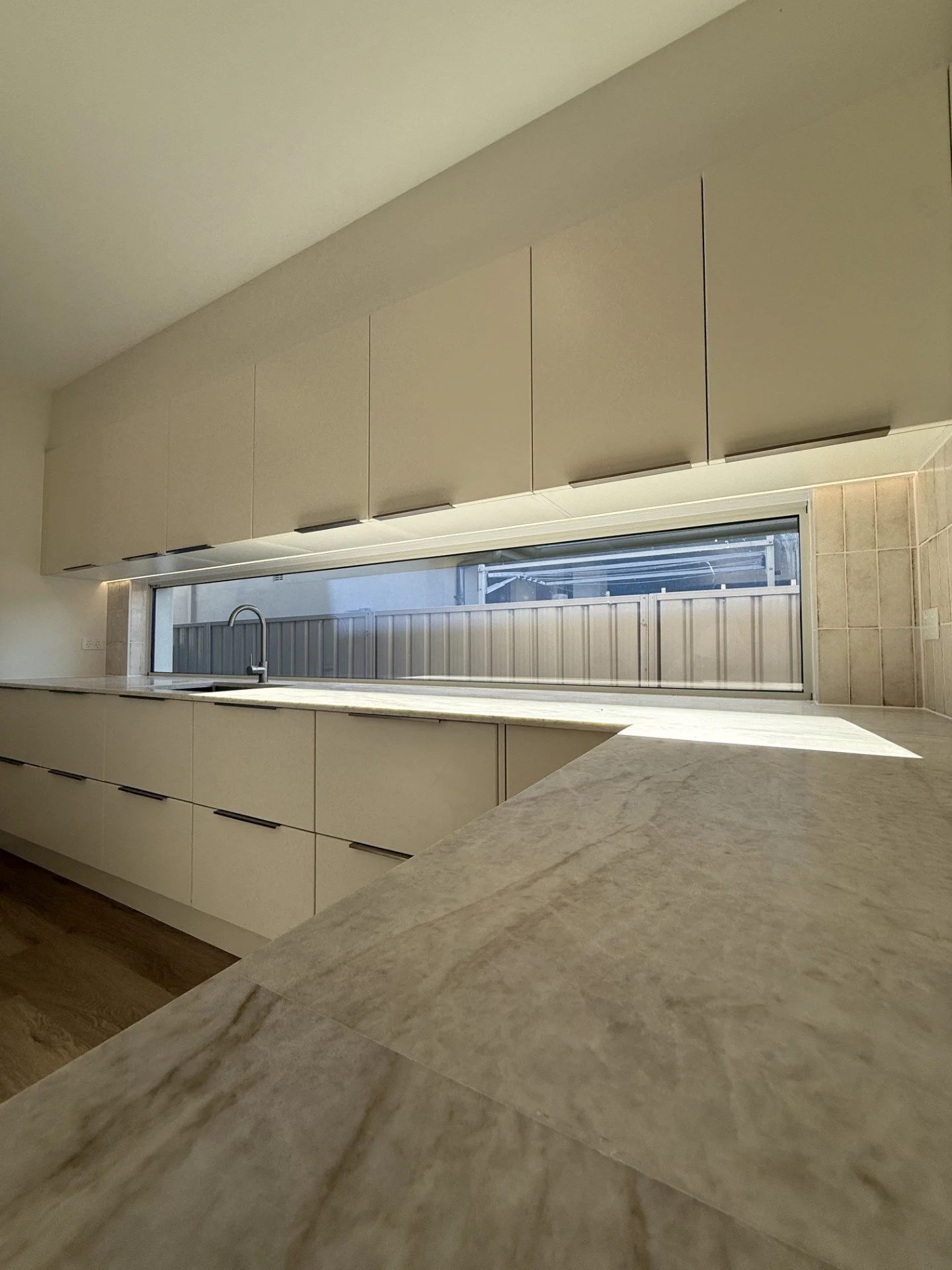 Modern kitchen with beige cabinets, a long horizontal window, and marble countertops.