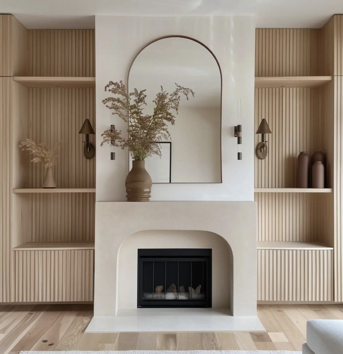 Living room with built-in wooden shelves, a white fireplace with a black grate, a large mirror, and decorative vases and lamps with neutral tones.
