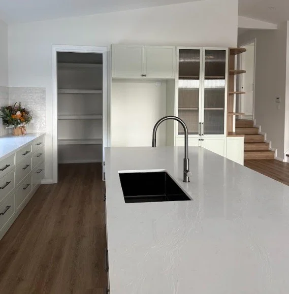 Modern kitchen with white cabinets, a large island with a sink and faucet, open shelving, and hardwood floors.