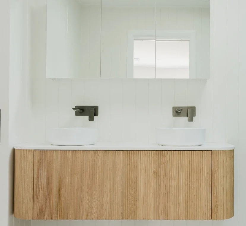 A modern bathroom vanity with two vessel sinks and wall-mounted faucets, with a mirror above and white shiplap walls.