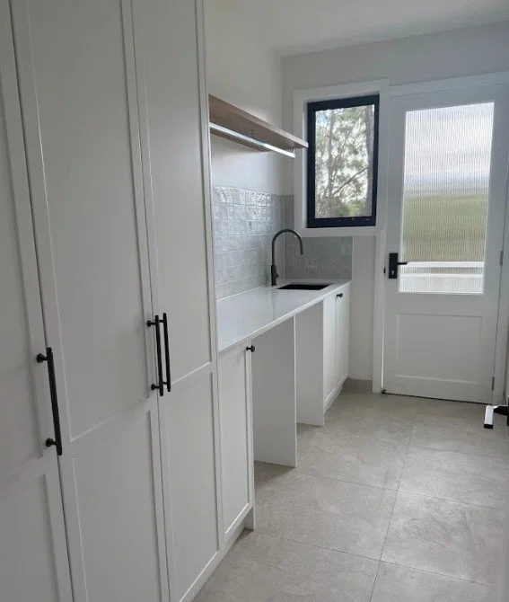 Small laundry room with white cabinets, a black sink faucet, a small window, and a door leading outside.