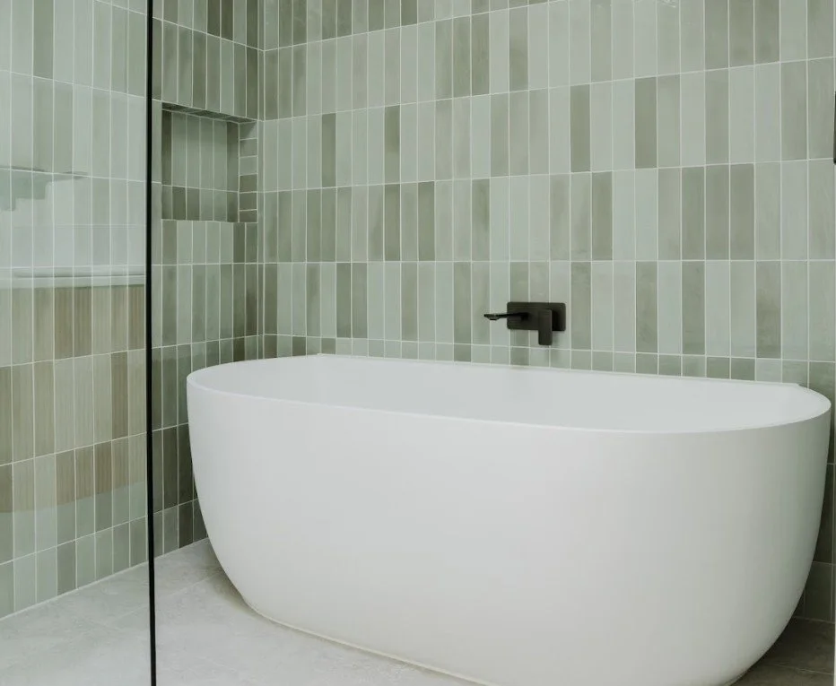 Modern bathroom with a white freestanding bathtub, green tiled walls, and a black wall-mounted faucet.