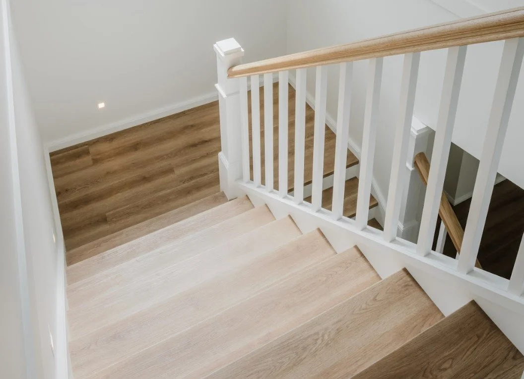 View of a staircase with light wood steps and a white railing with wooden handrails, leading to a lower level with a wood floor.