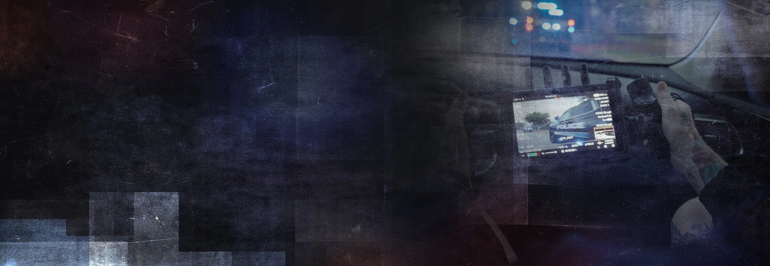 A police car is visible on a mobile device screen as the person takes a photo in the front car mirror. The scene outside appears to be in a parking lot on a rainy day.