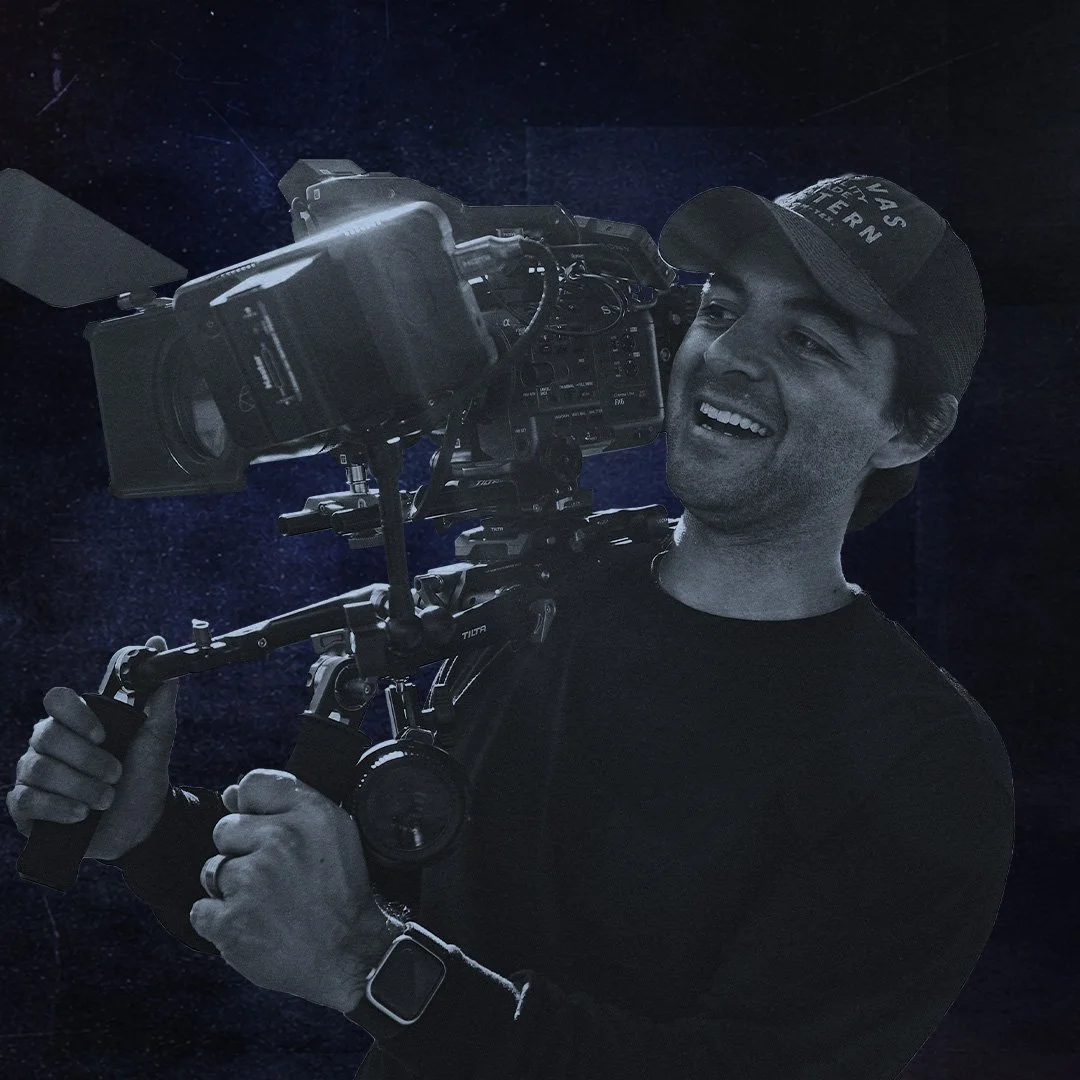A man smiling while holding a professional video camera in space-themed background.