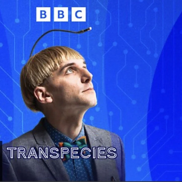 A picture of Neil Harbisson who is wearing a suit with a bow tie. He looks up to the antenna protruding from his head