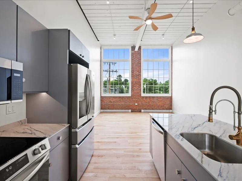 The Spinning Mill - Open-concept kitchen with large island, modern cabinetry, and industrial windows