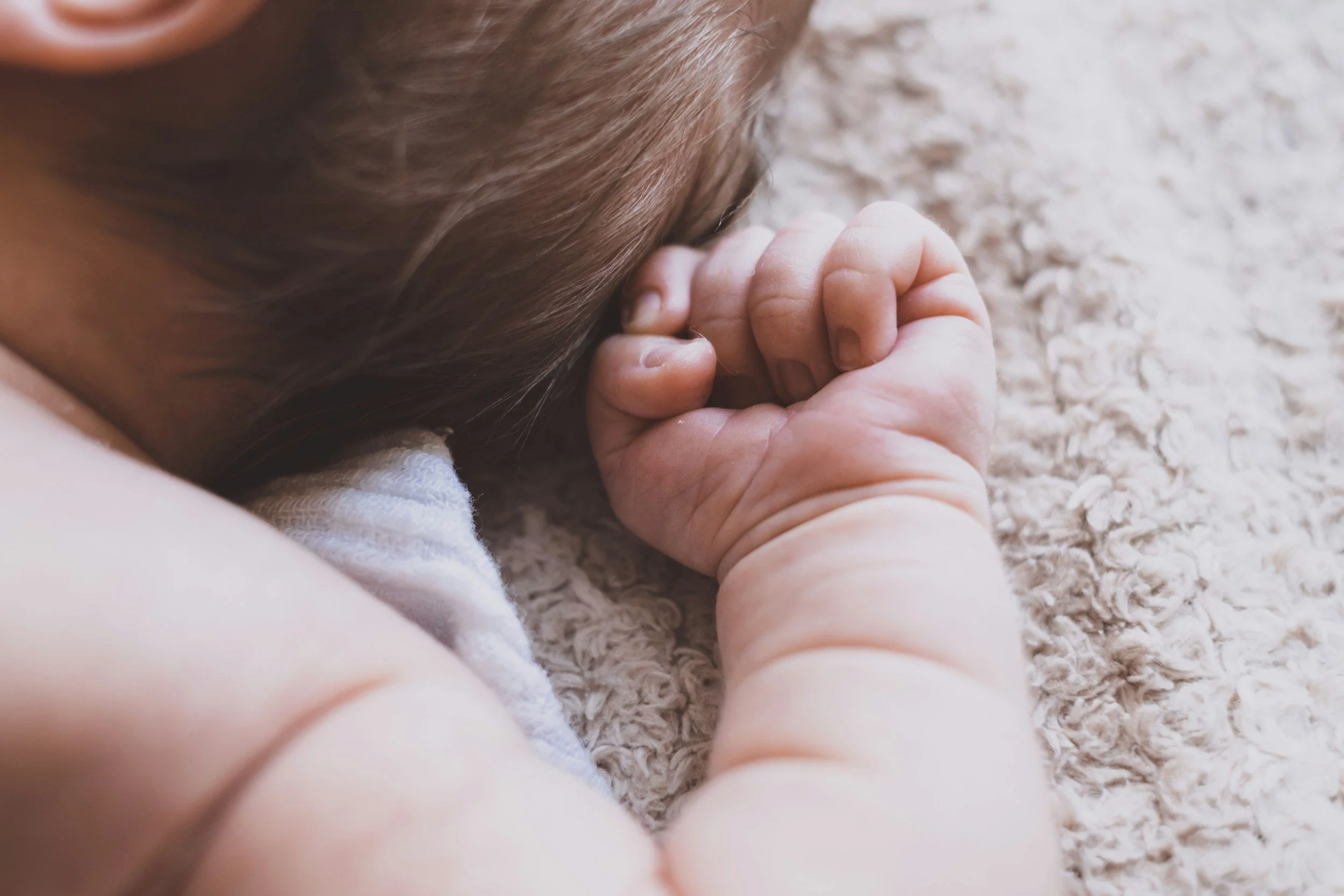 Close-up of a baby lying on a soft, textured blanket with their head resting on the blanket and one hand near their face.