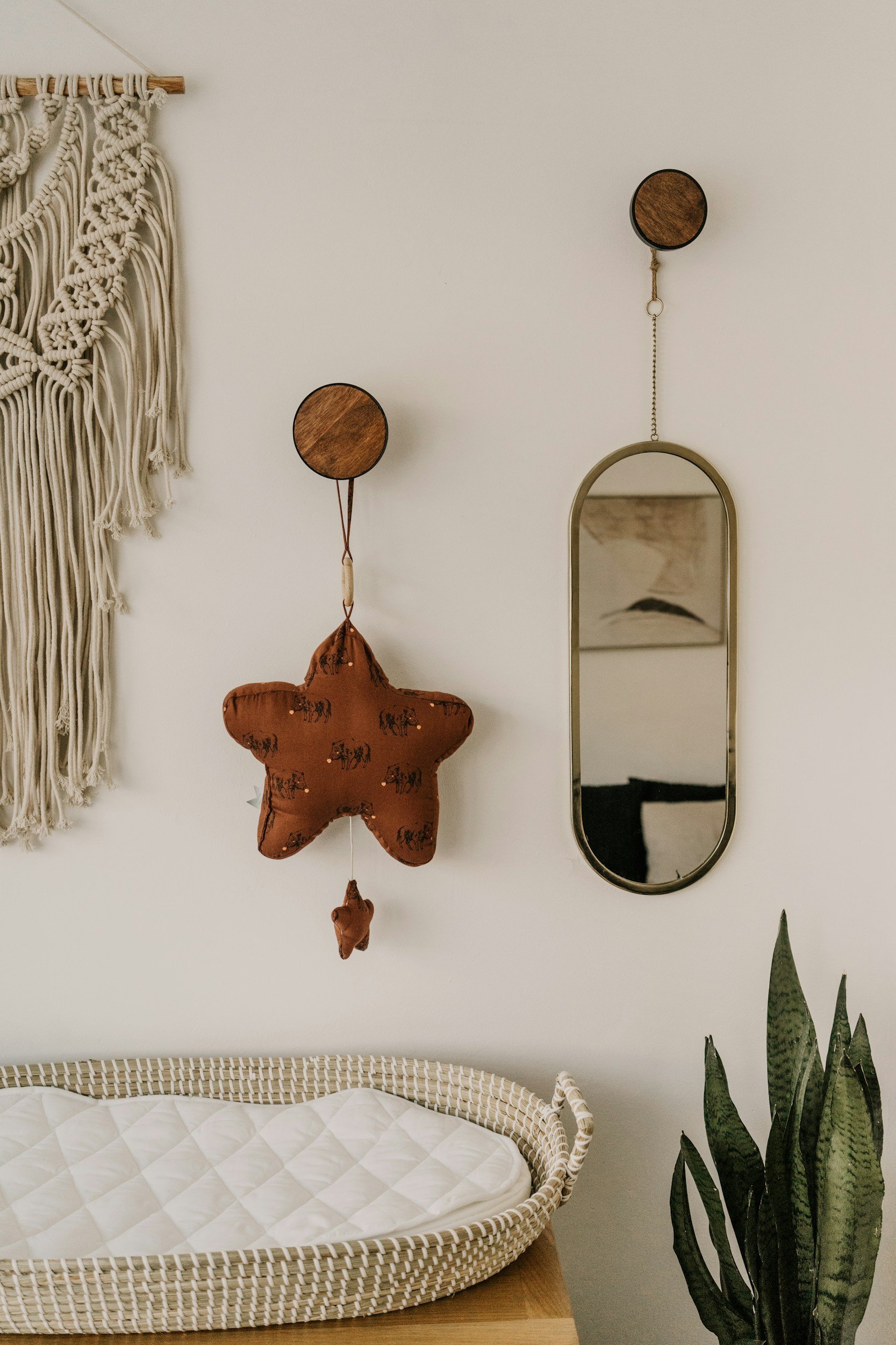Wall decor with macramé wall hanging, star-shaped stuffed toy, small oval mirror, and a potted plant next to a changing pad.