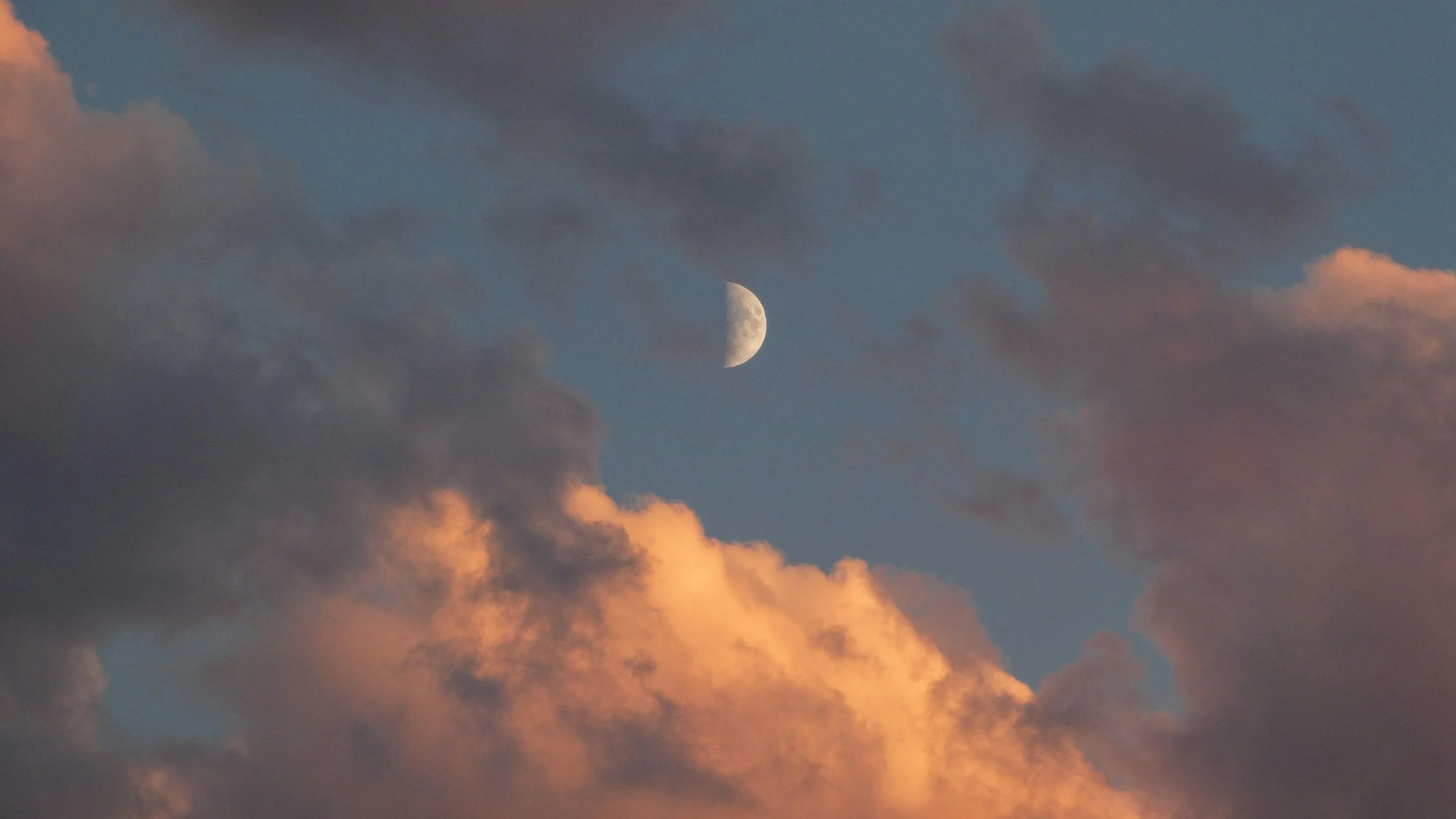 The moon visible through partially clouded sky at sunset.