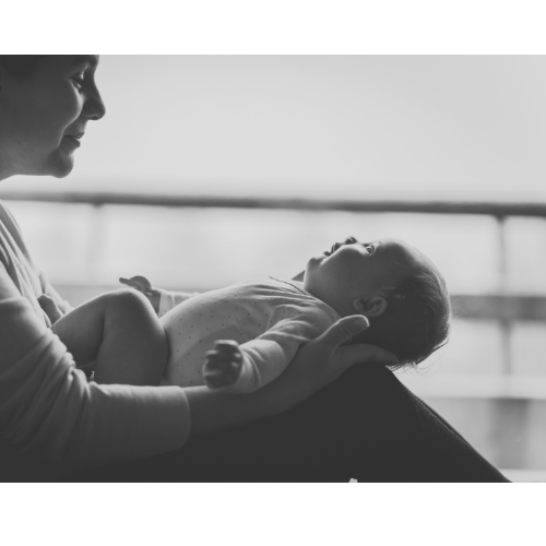 A woman holding a baby, smiling and looking at the baby, in a black-and-white indoor setting.
