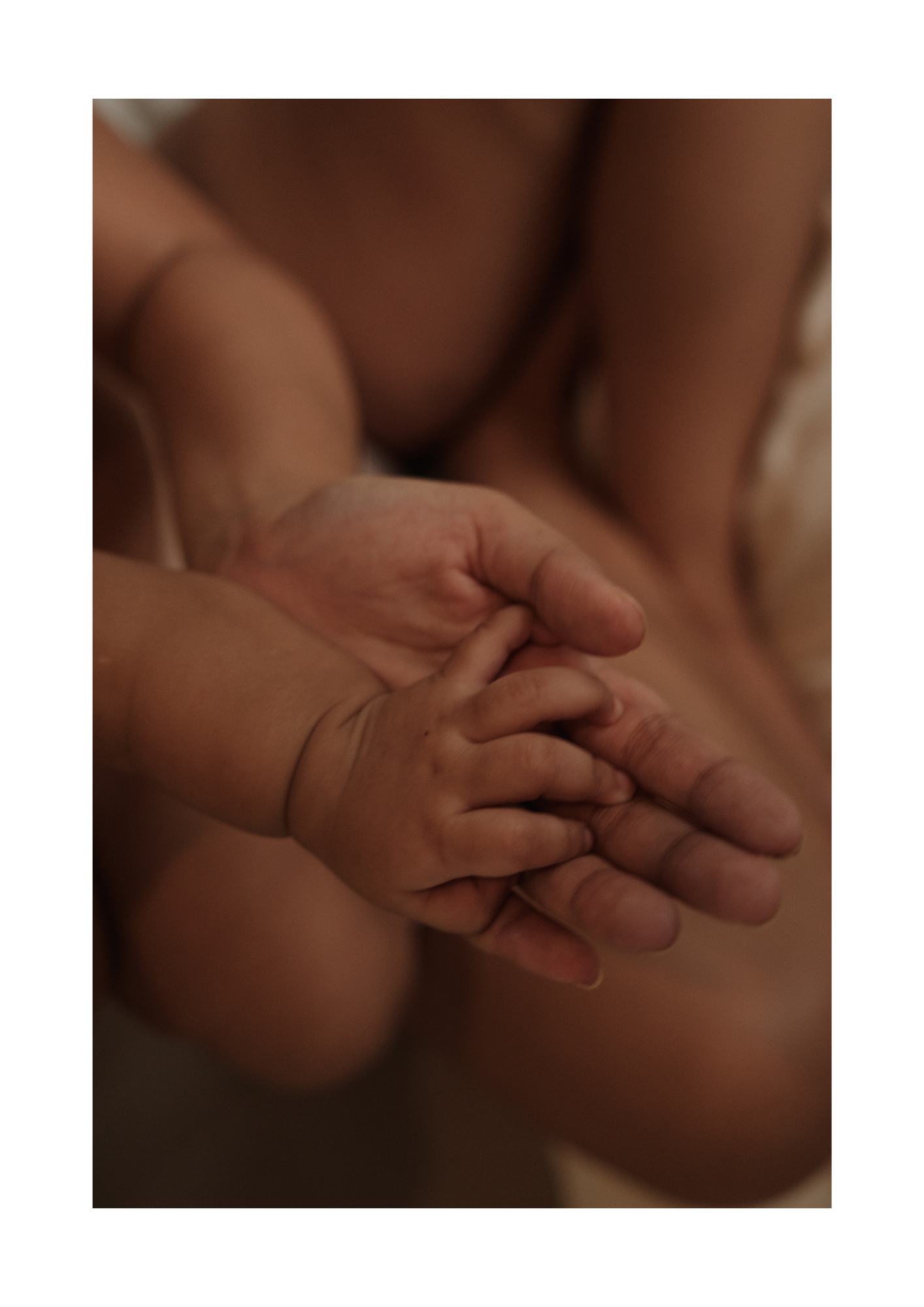 Close-up of a baby's hand grabbing an adult's finger, soft lighting and intimate setting.