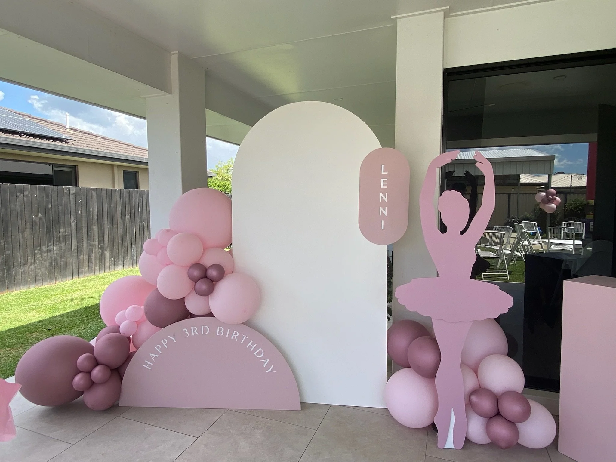 Decorations for a birthday celebration featuring pink and purple balloons, a pink ballerina cutout, and a sign that reads 'Happy 3rd Birthday' and 'Lennni'.