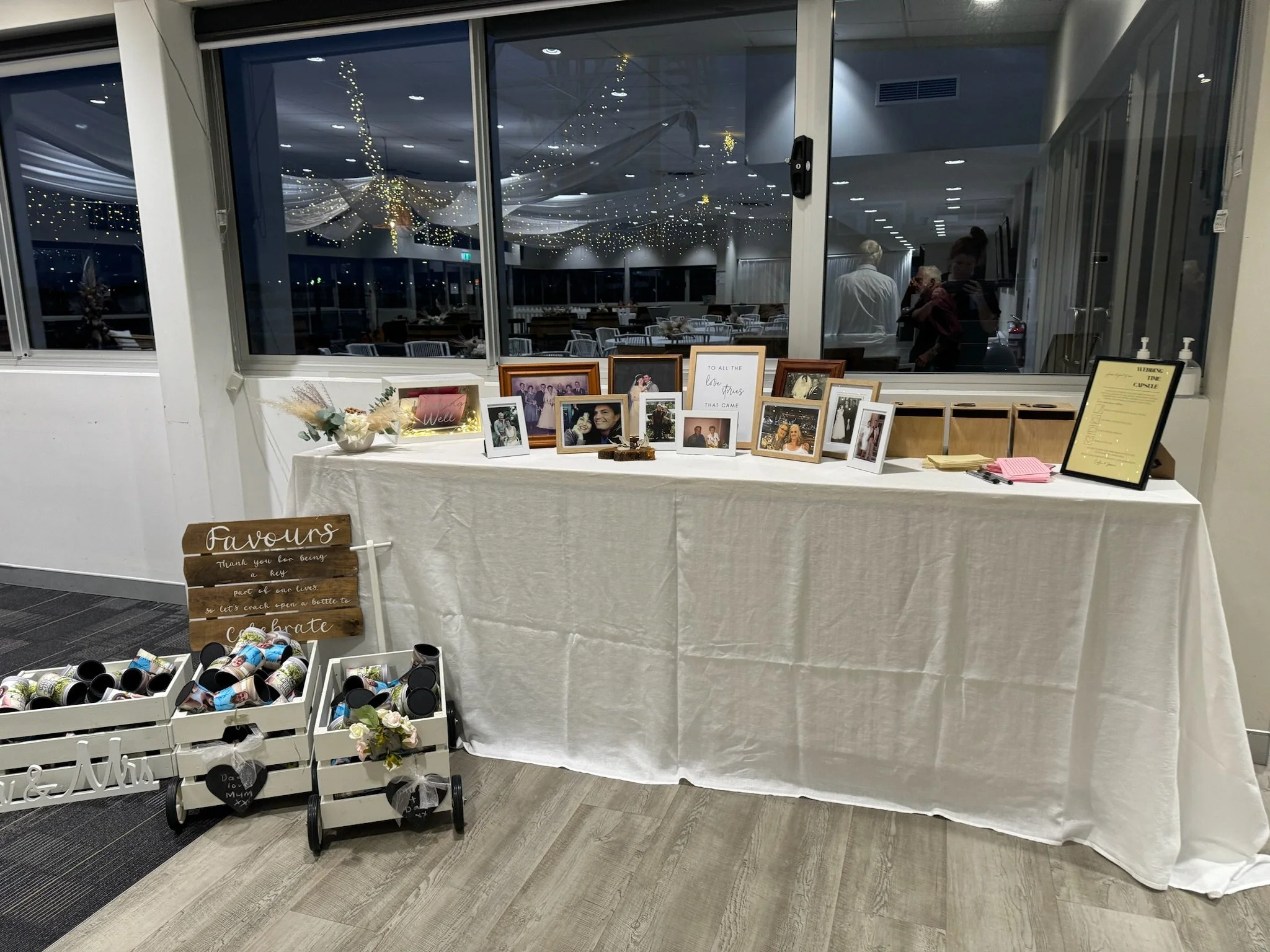 Wedding guestbook and photo display table with framed pictures and a sign reading 'Favours' at a wedding reception.