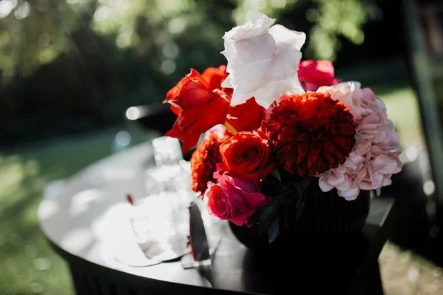 A bouquet of red, pink, and white flowers on a garden table with a blurred outdoor background.