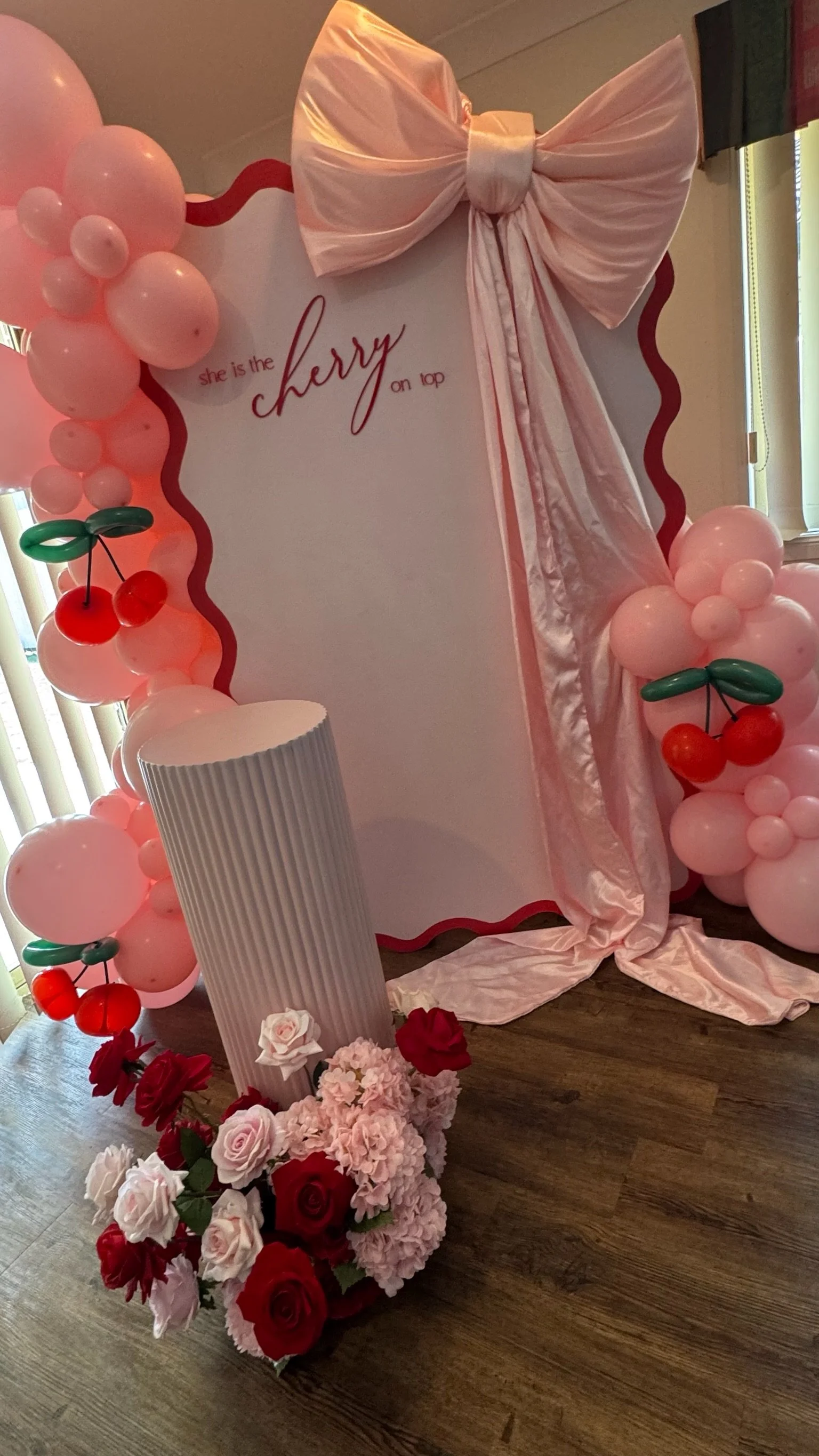 Decorative board with pink balloons, cherries, flowers, and a large pink bow, featuring the text 'she is the cherry on top' for a celebration or party.