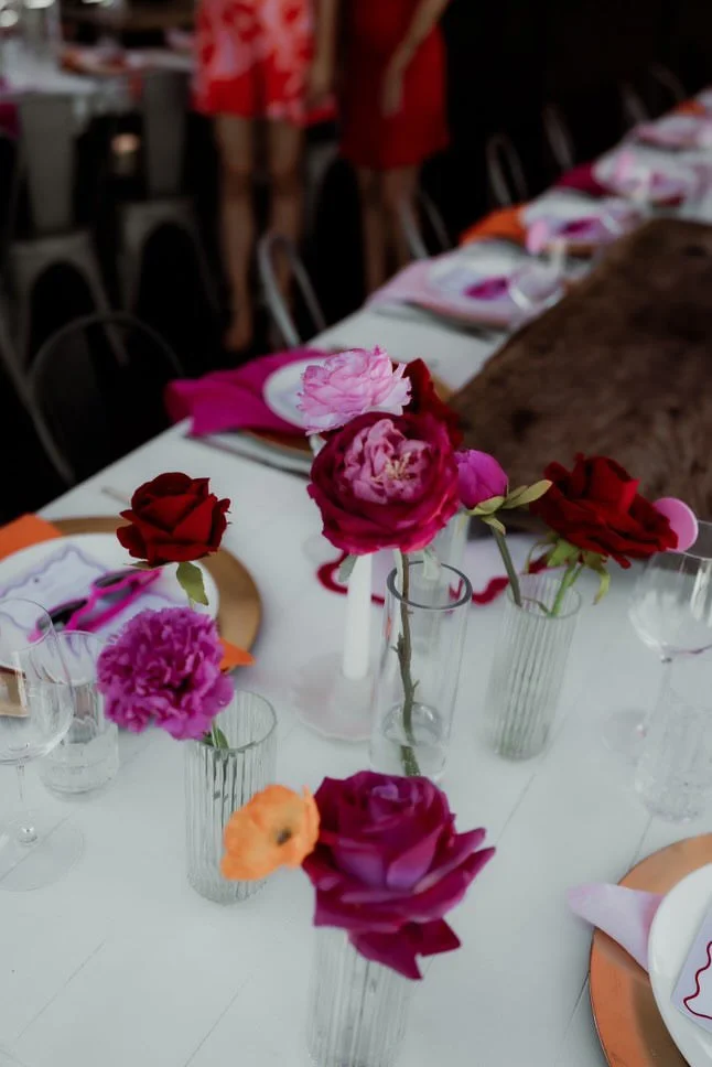 A table decorated with colorful flowers in vases, set with plates, glasses, and napkins, likely for a celebration or gathering.