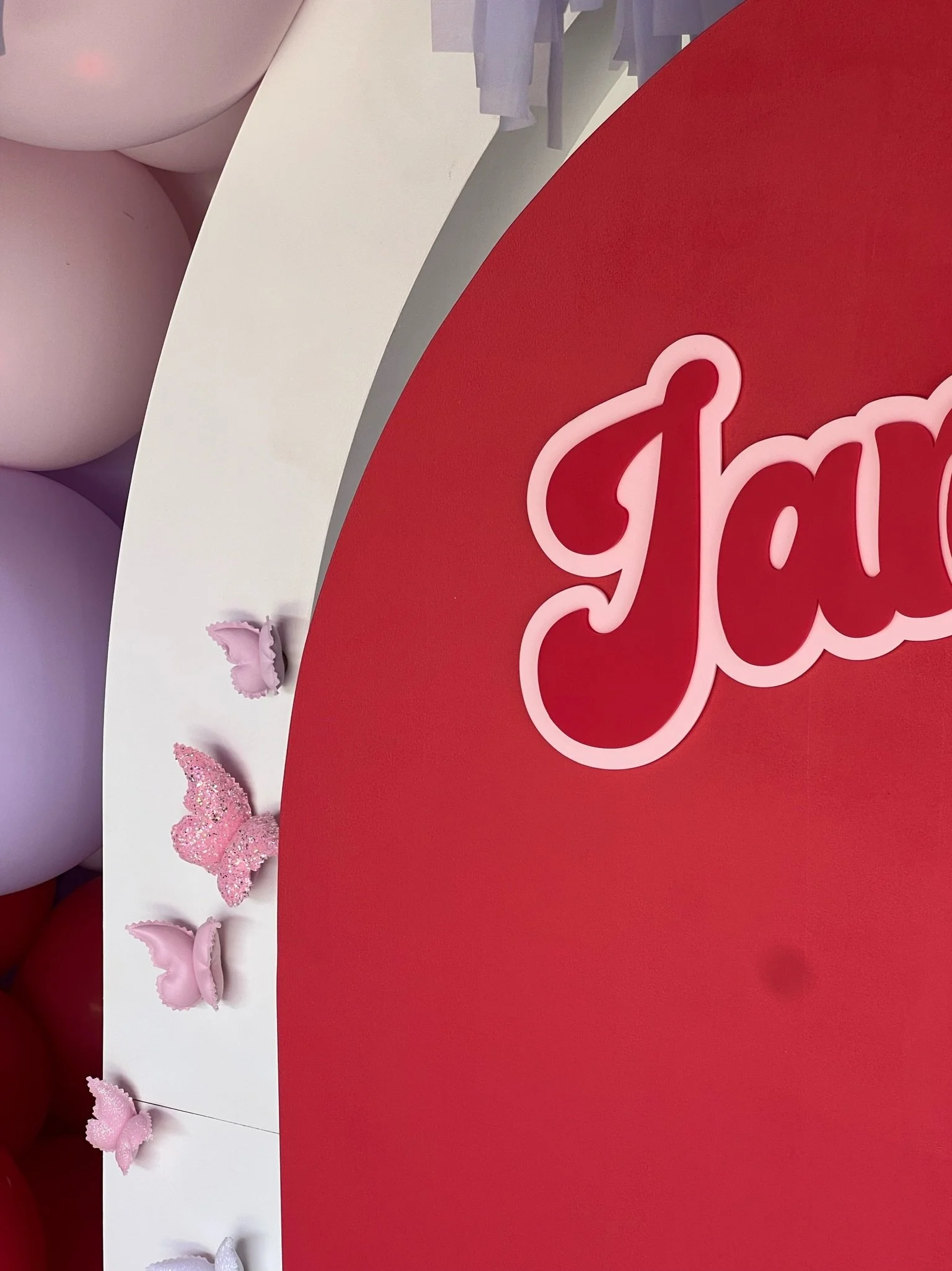 Close-up of a pink and red decorative display with pink butterfly and glitter ornaments, and cursive text partly visible reading 'G'.