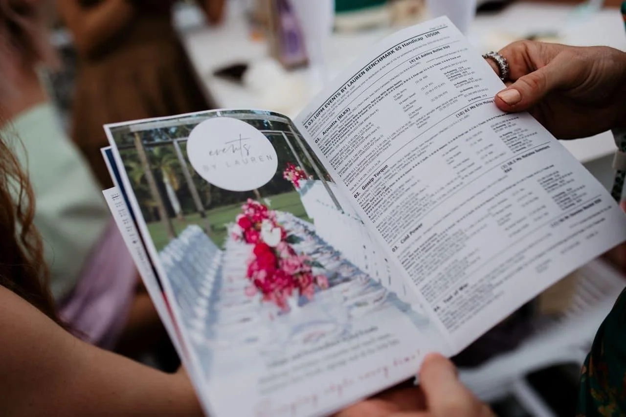 Person holding open a wedding program with wedding details, featuring a colorful floral image on left page.