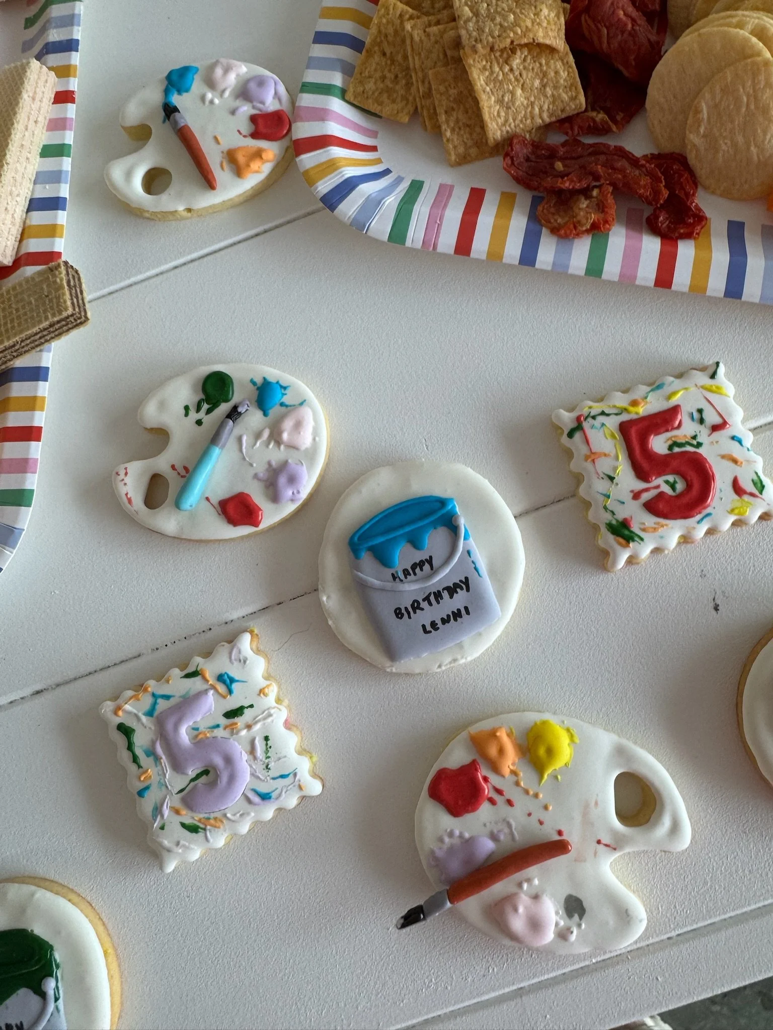 Decorative cookies themed for a birthday celebration, with paint palette shapes, a paintbrush, and birthday messages like 'Happy Birthday Leni'.