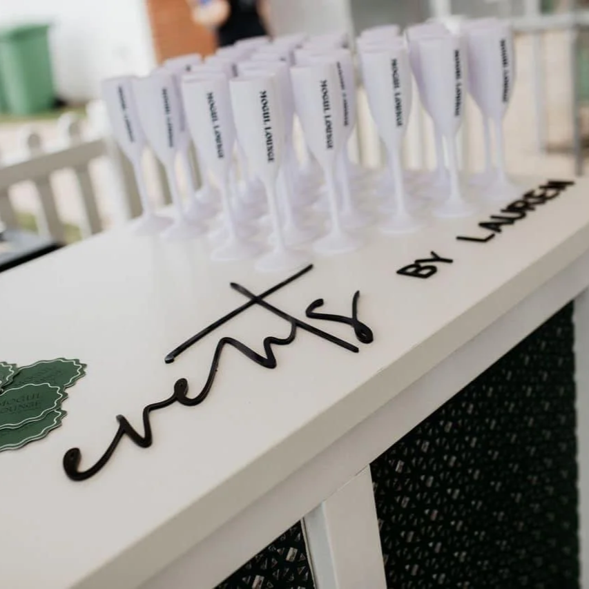 Champagne glasses with labels on a white table with black cursive writing that says 'champagne by Laura'.