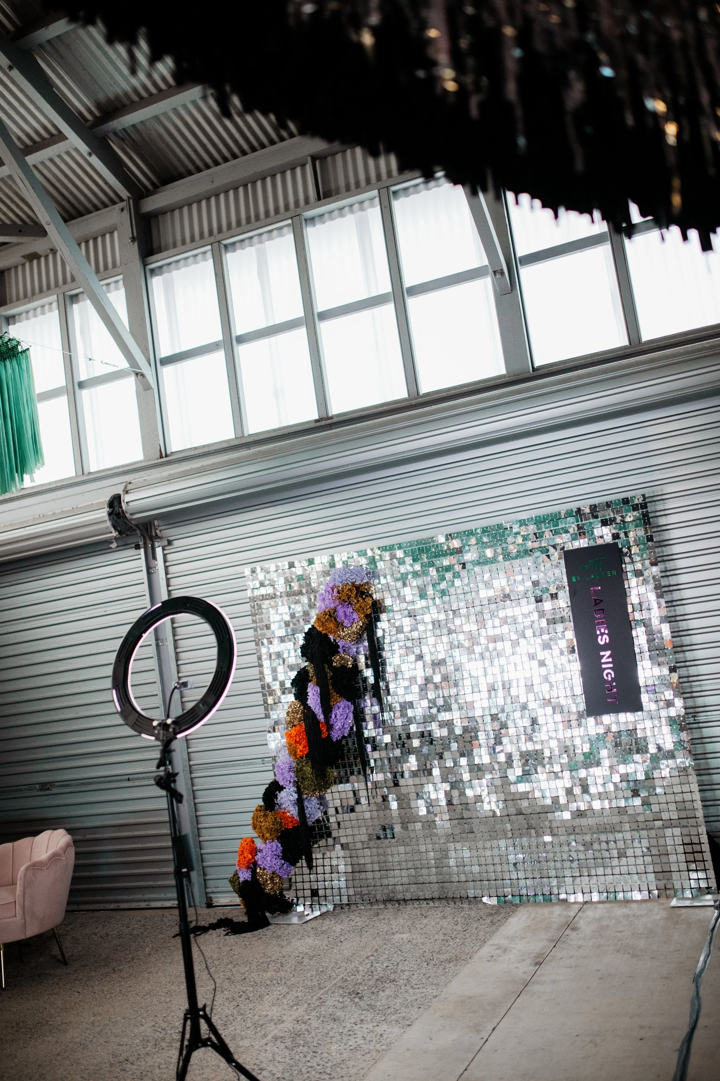 Decorative display with a mirrored mosaic backdrop, floral arrangement, and sign reading 'Ladies Night,' set up in an industrial interior space.