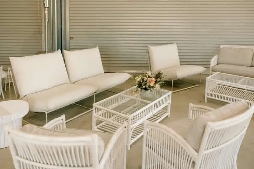 Indoor waiting area with white sofas, chairs, wicker tables, and a flower arrangement.