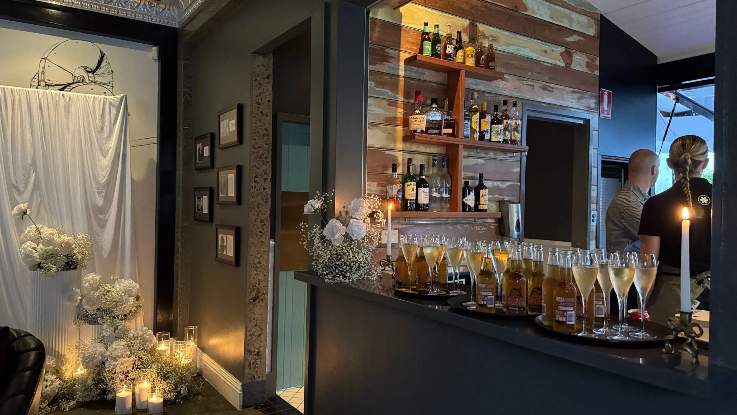 Decorated bar area at a celebration with champagne glasses, bottles of liquor, and floral arrangements with candles.