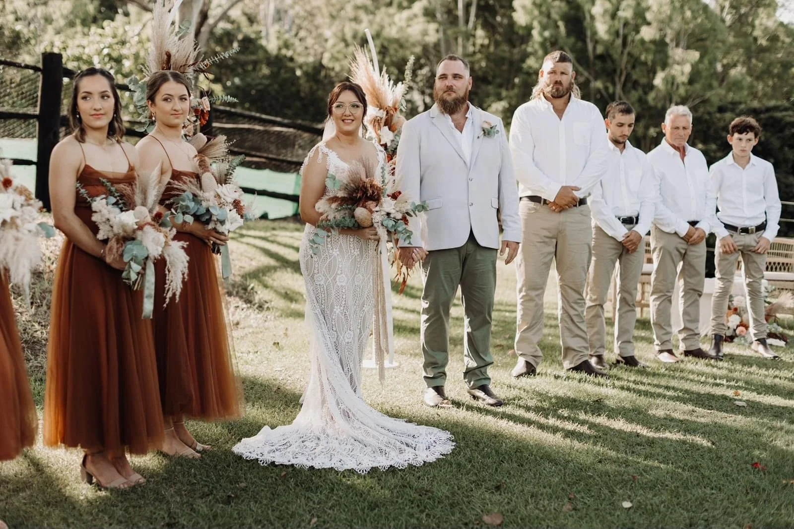 A wedding ceremony outdoors with the bride and groom holding hands, standing among bridesmaids and groomsmen.