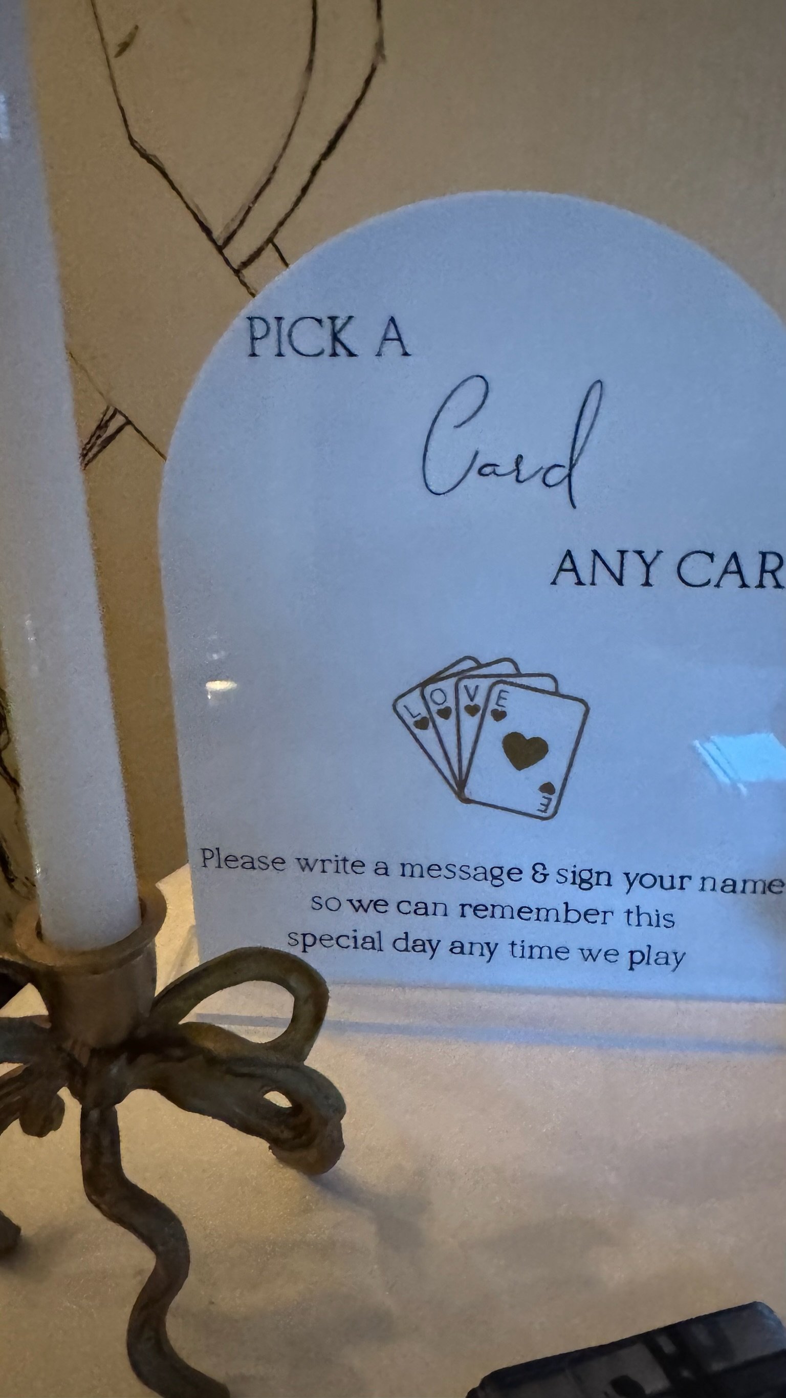 Sign encouraging guests to pick a card from a deck for a special memory, with a candle holder in the foreground.