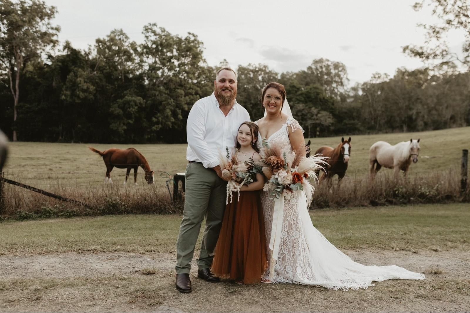 A family celebrating a wedding outdoors with horses grazing in the background on a grassy field.
