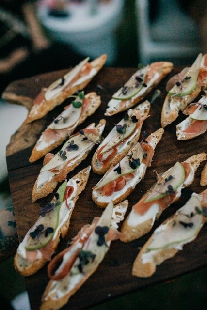 Variety of gourmet crostinis with toppings such as smoked salmon, cheese, and herbs on a wooden serving board.