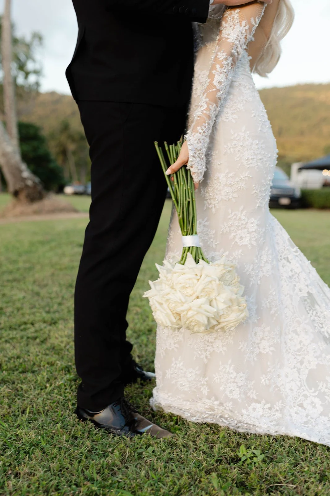 Close-up of a bride and groom standing outdoors, with the bride holding a bouquet of white roses.