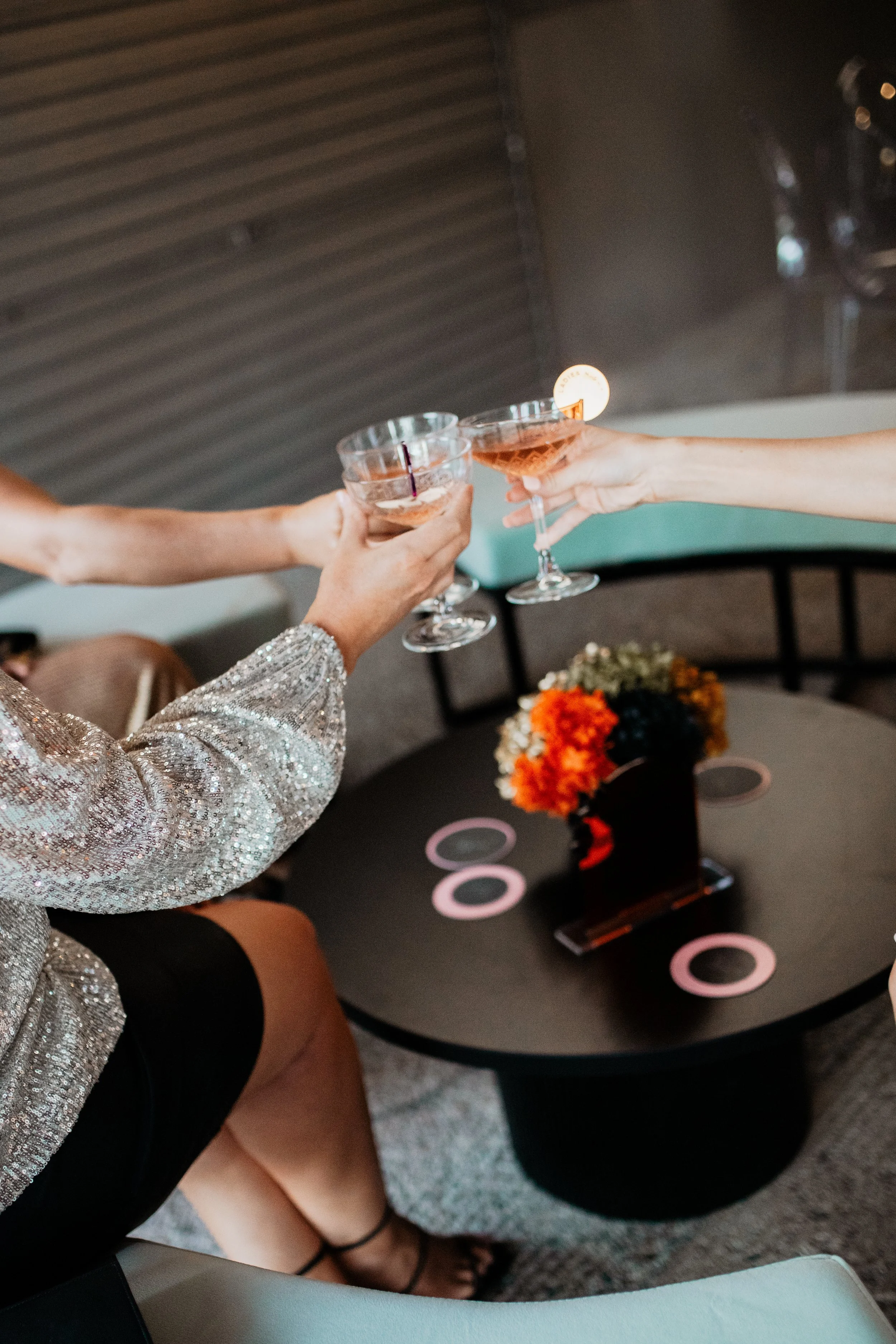 Three women holding glasses of pink cocktails for a toast at a table with a floral centerpiece.