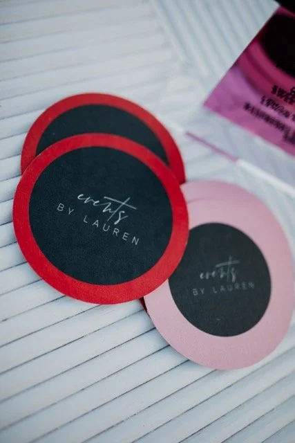 Three round coasters with the text "crafts BY LAUREN" on a striped surface, with pink and black colors.