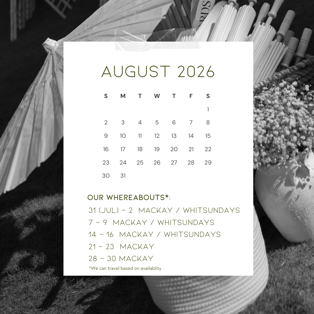 A calendar for August 2026 overlaid on a black and white photo of a picnic setup with a basket, flowers, and paper umbrellas.
