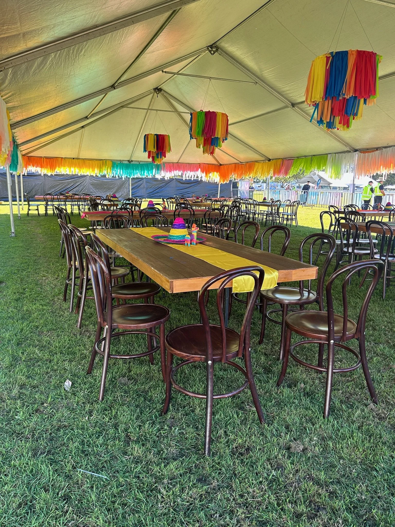 Decorated outdoor event tent with tables, chairs, colorful hanging streamers, and sombrero hats on the tables for a fiesta celebration.