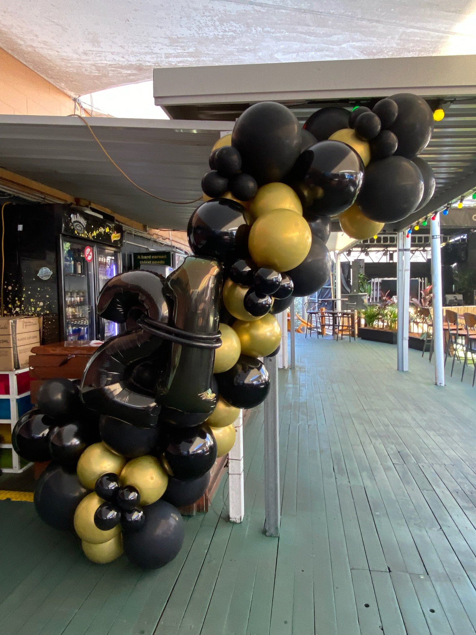 Decorative black and gold balloons arranged with large metallic balloon numbers and letters at an outdoor venue.
