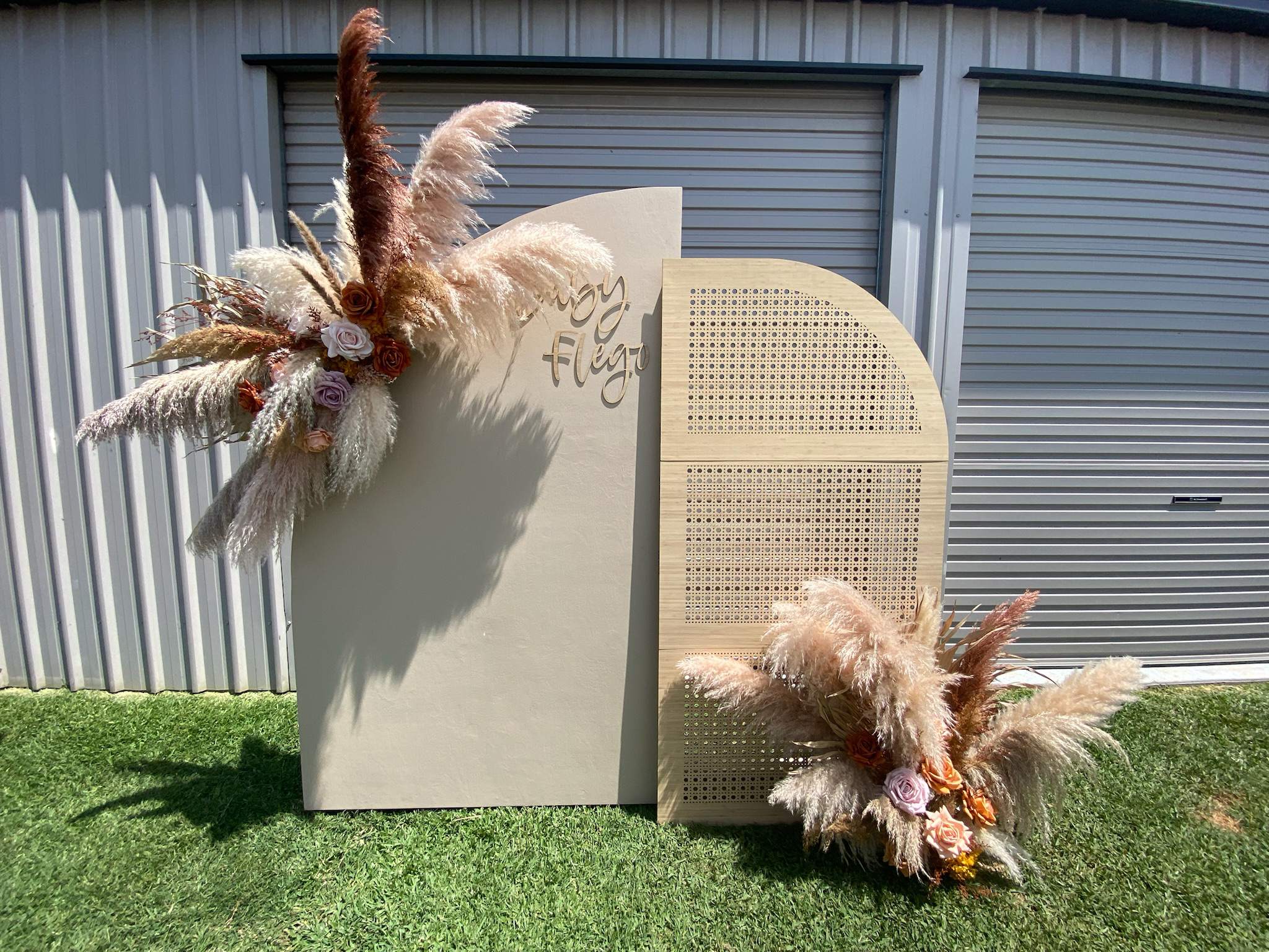 Decorative photo display featuring pampas grass and roses attached to a wooden and beige backdrop, with the words "Enjoy the Flare" cut out in script.