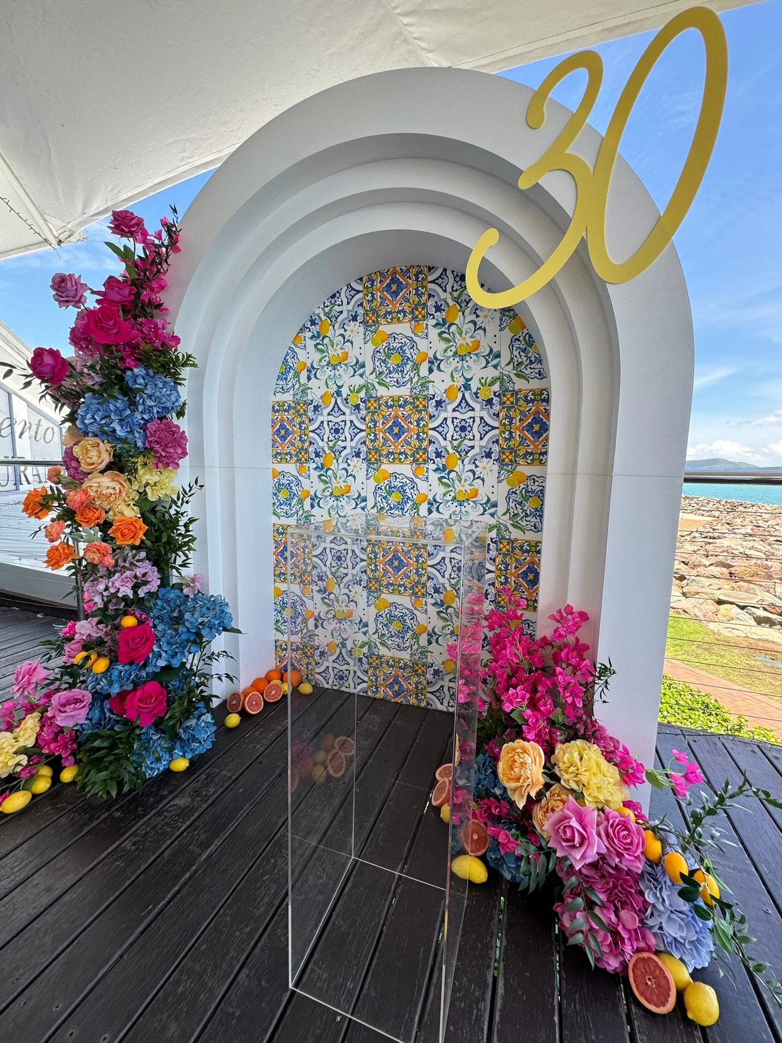 Decorative arch with colorful floral arrangements, citrus fruits, and tiles with intricate blue, yellow, and white patterns, celebrating a 30th birthday.