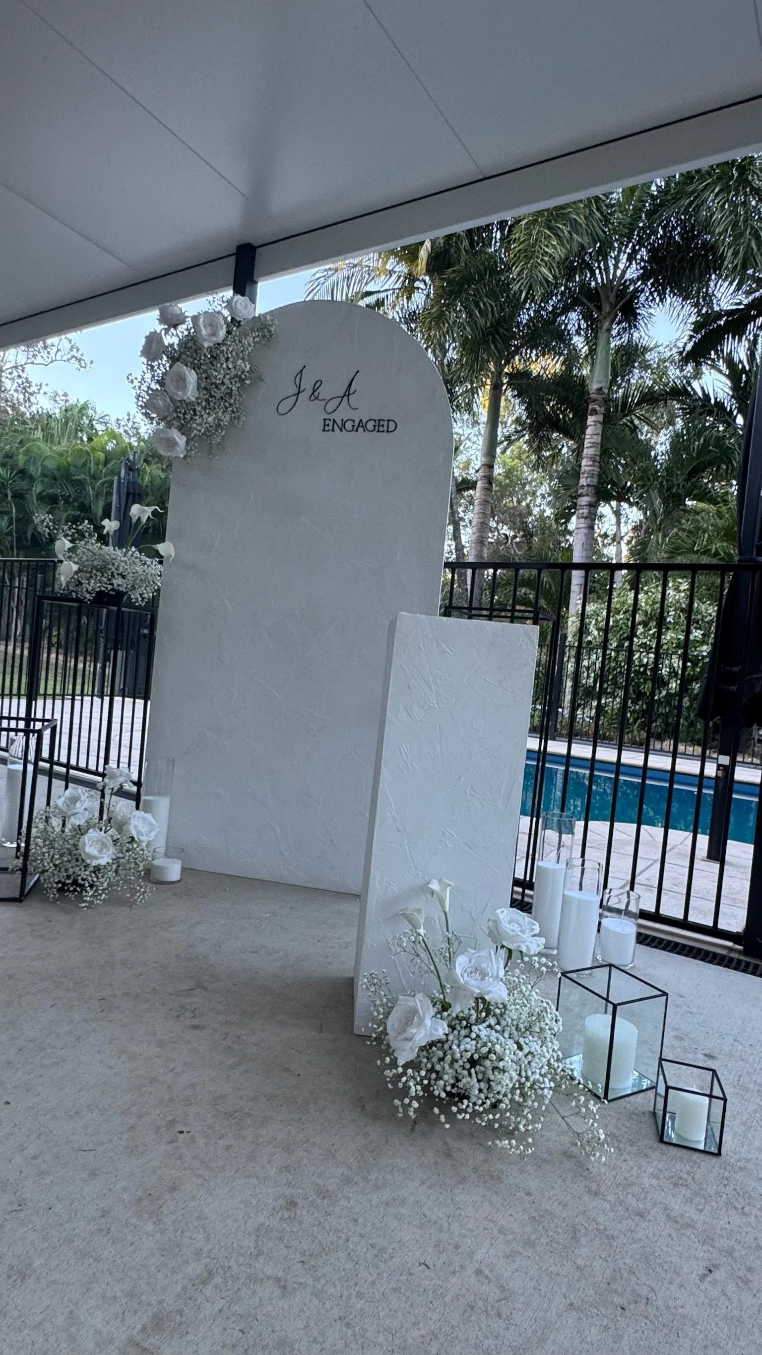 Decorative wedding or engagement backdrop with white flowers, candles, and greenery, indicating an engagement celebration.