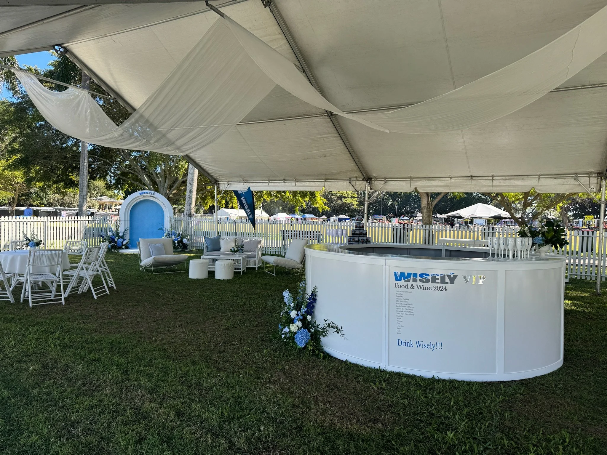 Party tent with white furniture, floral arrangements, and a blue and white theme for Wisely Food & Wine 2024 event.