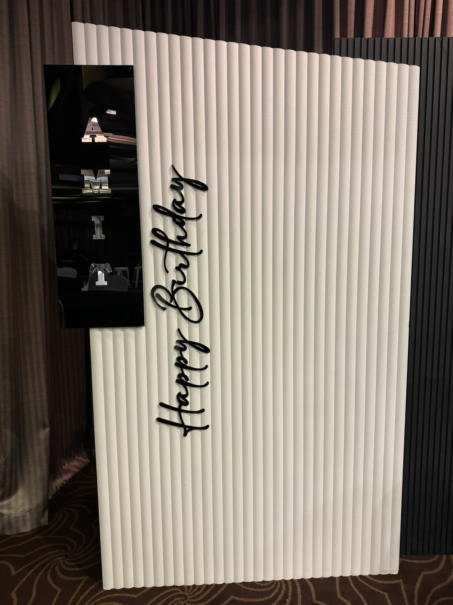 Sign with the words 'Happy Birthday' in cursive black font, mounted on a vertically striped white background.