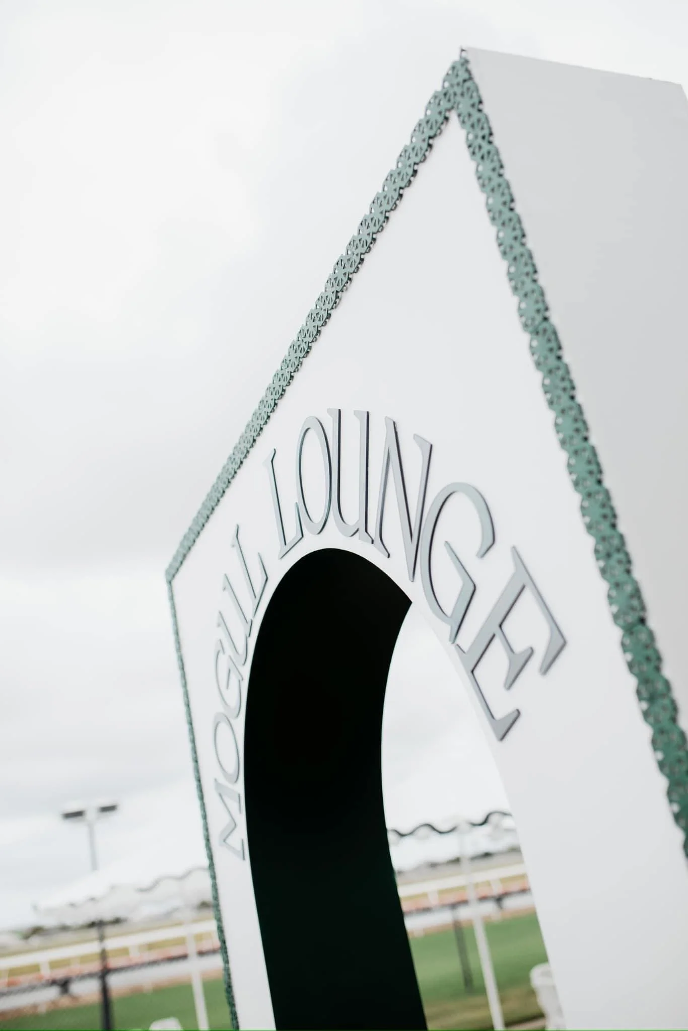White sign with the word "ALL YOUTH" in large raised letters, with a black circular opening or cutout, and a decorative border on the top and side edges, standing outdoors on cloudy day.