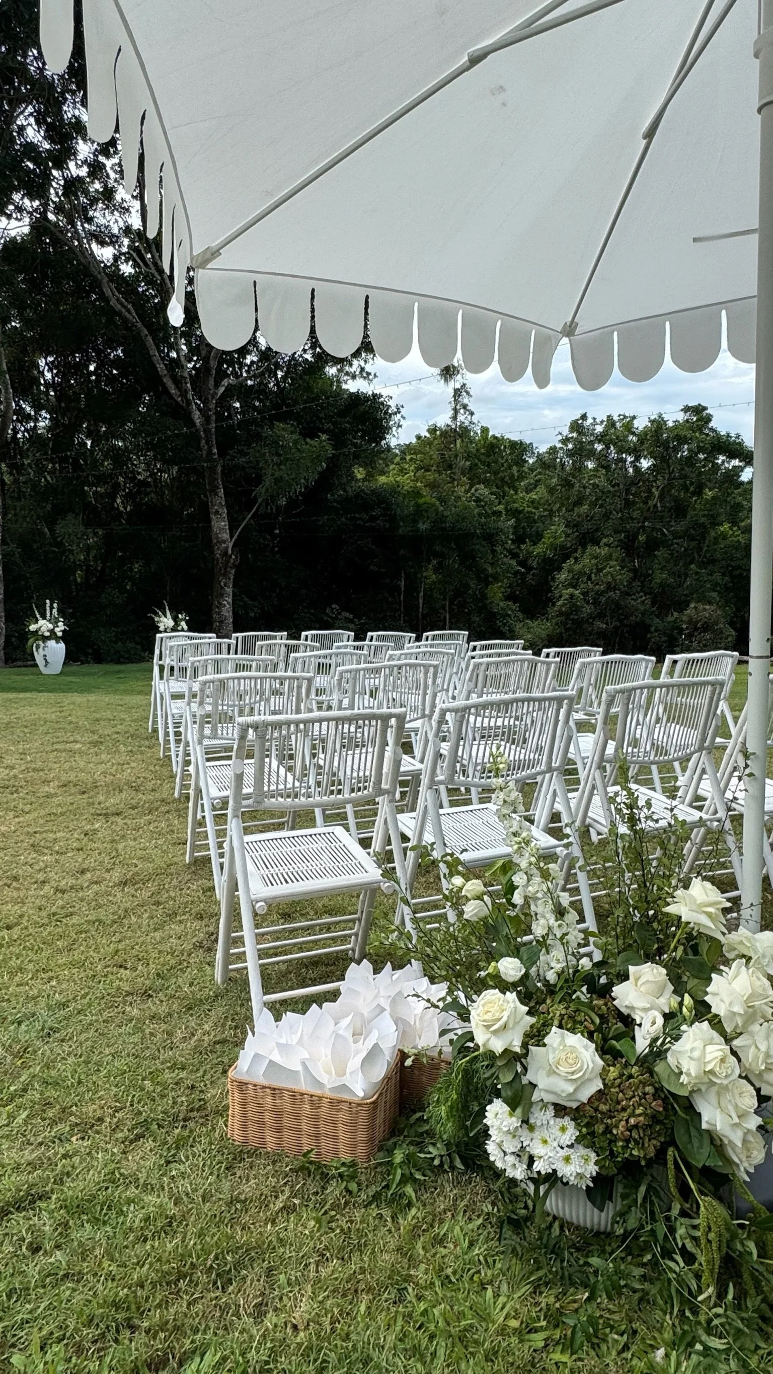 Outdoor wedding ceremony setup with white chairs, floral arrangements, and a large white patio umbrella.
