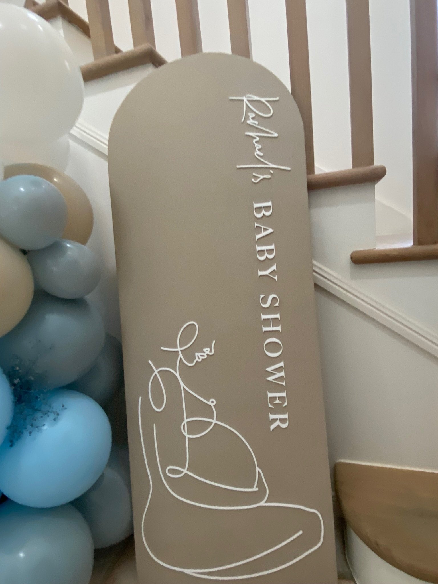 Decorative sign reading 'Proudly's Baby Shower' and 'Love' with a line drawing of a baby in a heart shape, next to a cluster of pastel-colored balloons.