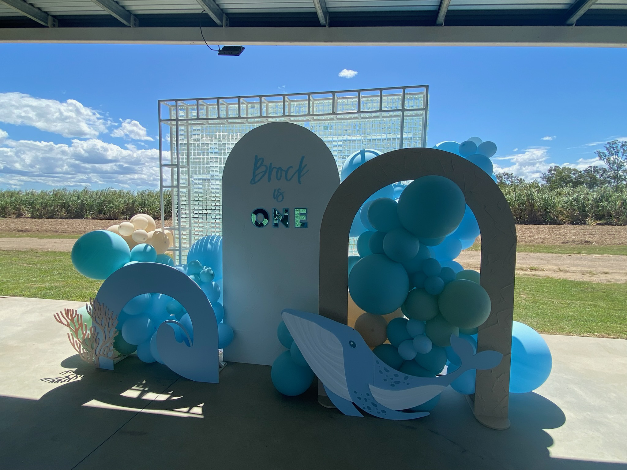 Decorative signs and balloons in blue and white with an ocean theme for a first birthday celebration outdoors.