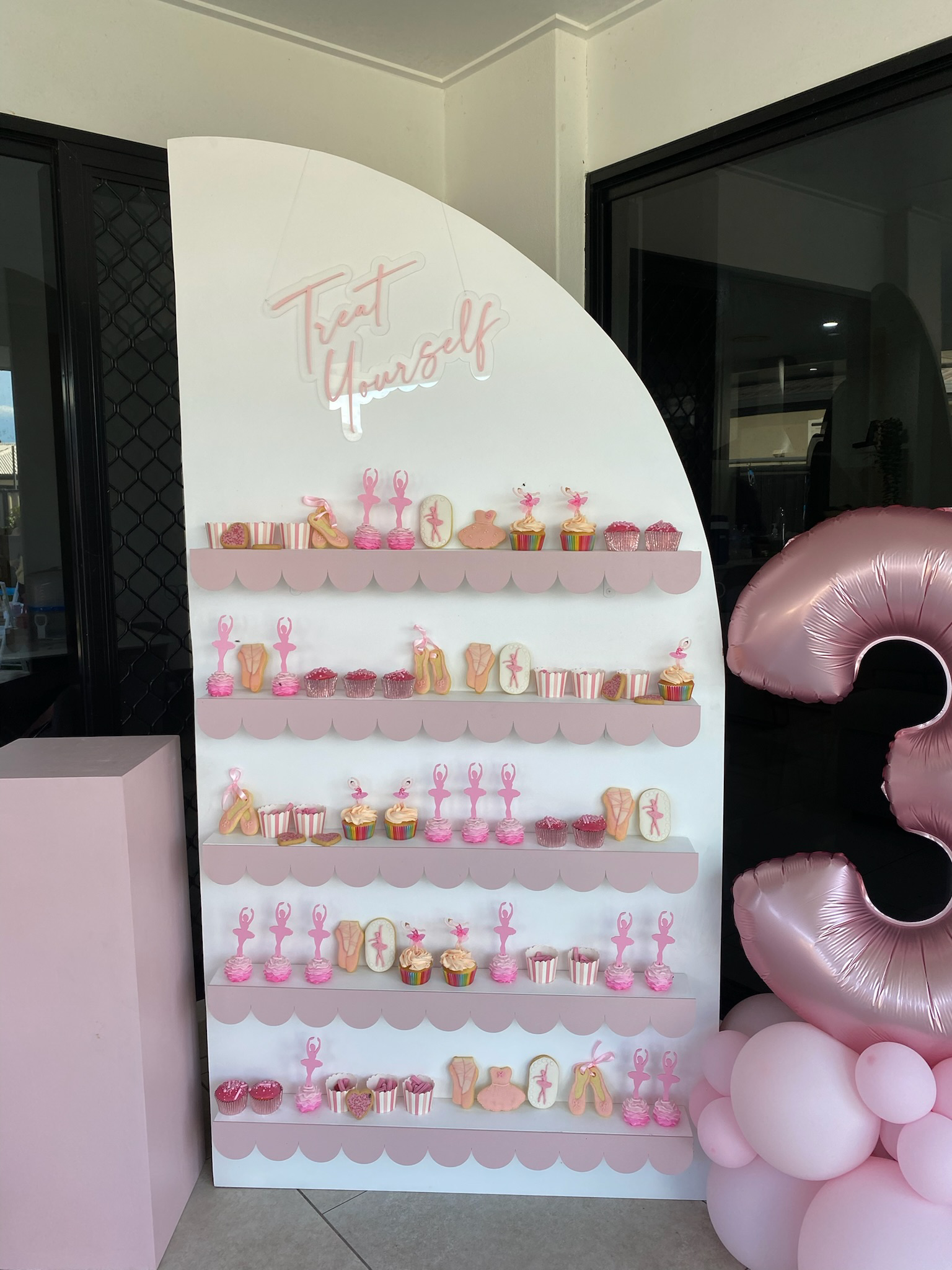 Decorative display board with pink and white desserts and the words 'Treat Yourself' sign at the top, with pink balloons on the right side.