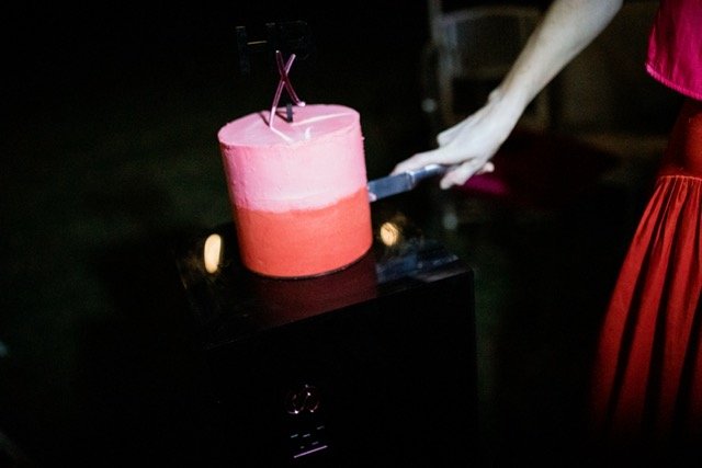 A person cutting a pink and red layered cake with a knife.