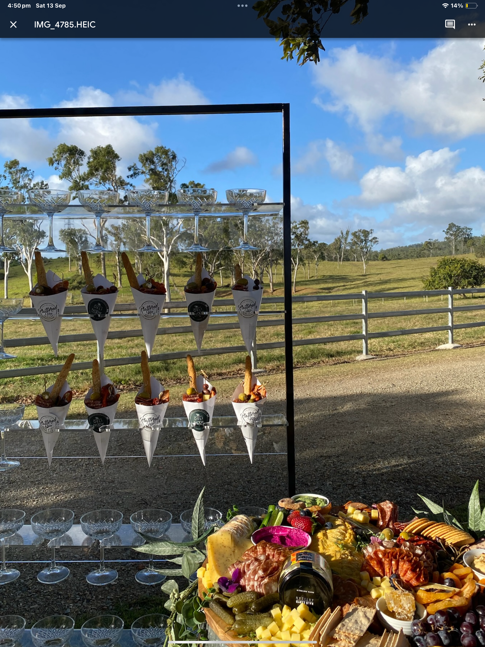 Outdoor food and drink display with glasses and ice cream cones against a rural landscape with blue sky, some clouds, green trees, and a white fence.